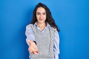 Genç esmer kadın mavi arka planda duruyor. Gülümsüyor, avuç içi dolusu yardım ve kabullenme teklif ediyor.. 