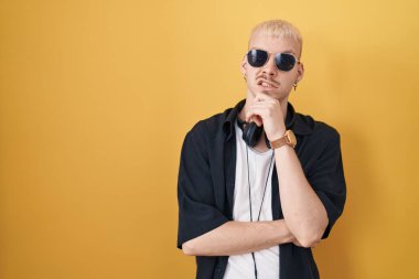 Sarı arka planda duran güneş gözlüğü takan genç beyaz adam bir soru hakkında endişeli ve gergin bir şekilde düşünüyor. 