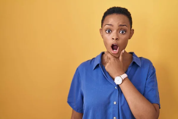 Stock image African american woman standing over yellow background looking fascinated with disbelief, surprise and amazed expression with hands on chin 