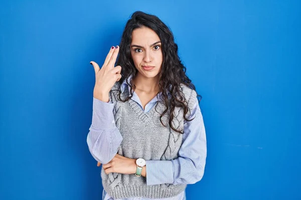 年轻的黑发女子站在蓝色背景的旁边 用枪指着自己的头和手指开枪自杀 — 图库照片