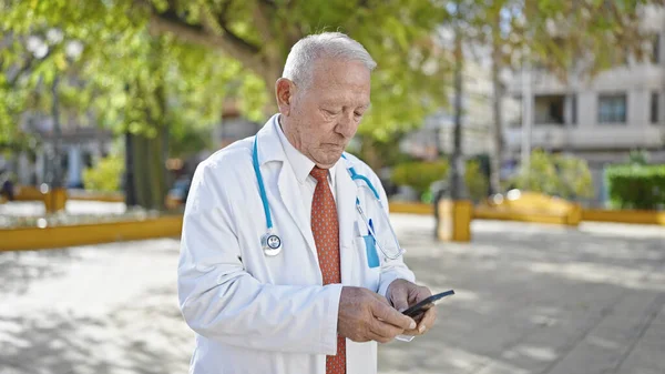 Senior Doctor Canoso Pie Con Expresión Seria Usando Teléfono Inteligente — Foto de Stock