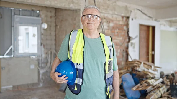 中年白发苍苍的建筑工人微笑着 自信地在建筑工地拿着硬礼帽 — 图库照片