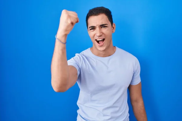 Молодой Латиноамериканец Стоящий Синем Фоне Злой Безумный Поднимающий Кулак Расстроенный — стоковое фото