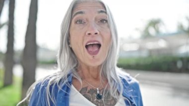 Parkta sürpriz bir ifadeyle duran orta yaşlı gri saçlı kadın.