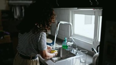 Orta yaşlı İspanyol kadın mutfakta tabak yıkıyor.