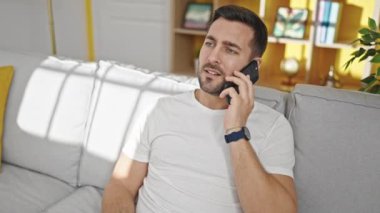 Genç İspanyol adam akıllı telefondan konuşuyor. Evdeki kanepede oturuyor.