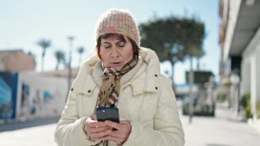 Ciddi bir ifadeyle caddede akıllı telefon kullanan olgun İspanyol kadın.