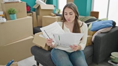 Genç ve güzel İspanyol kadın yeni evindeki kanepede oturmuş belge okuyor.