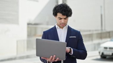 Genç Latin iş adamı sokakta dizüstü bilgisayarı kapatıyor.