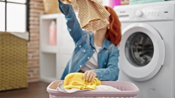 若い赤毛の女性が洗濯室で服を分離床に座って — ストック動画
