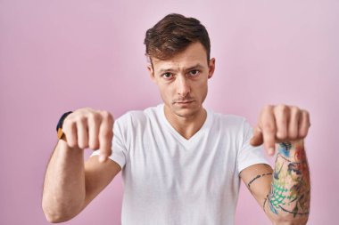 Pembe arka planda duran beyaz adam üzgün ve üzgün görünüyor, parmaklarıyla yönü gösteriyor, mutsuz ve depresif.. 