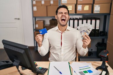 Sakallı genç İspanyol bir adam küçük işletme ecommerce çalışıyor. Elinde banknotlar ve kredi kartı var. Öfkeli ve öfkeli çığlıklar atıyor.. 