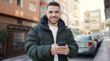 Young hispanic man smiling confident using smartphone at coffee shop terrace