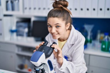 Adorable girl scientist using microscope working at laboratory