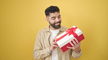 Genç İspanyol adam gülümsüyor. Sarı arka planda kendine güvenen bir hediye tutuyor.