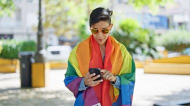 Parkta gökkuşağı bayrağı takan güzel İspanyol kadın akıllı telefon kullanıyor.