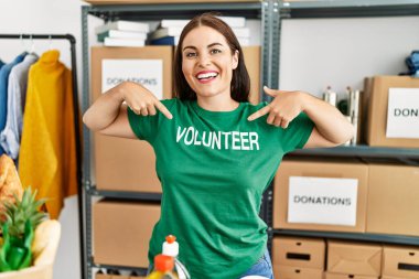 Genç, güzel, İspanyol bir kadın gülümsüyor. Yardım merkezinde gönüllü tişört giyecek birini işaret ediyor.