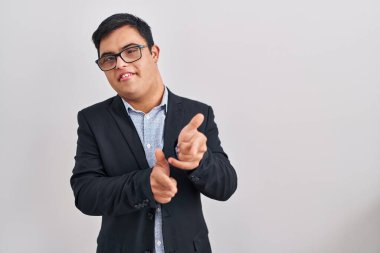 Down sendromlu genç İspanyol adam iş stili giyinip mutlu ve komik yüzlü parmaklarını kameraya doğrultuyor. iyi enerji ve titreşimler. 