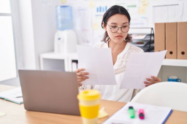 Young hispanic woman business worker using laptop reading document at office