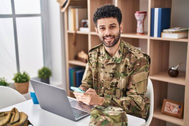 Young arab man army soldier using laptop using smartphone at home