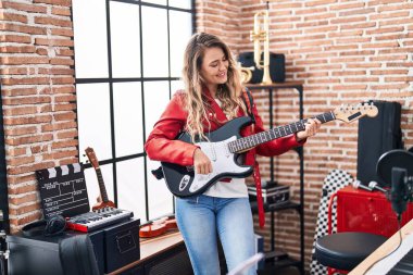 Young woman musician playing electrical guitar at music studio