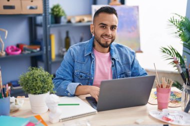 Genç İspanyol ressam resim stüdyosunda dizüstü bilgisayar kullanıyor.