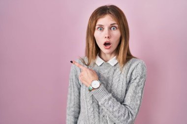 Pembe arka planda duran güzel bir kadın parmaklarını yana doğru göstererek şaşırdı, ağzı açık hayret içinde kaldı.. 