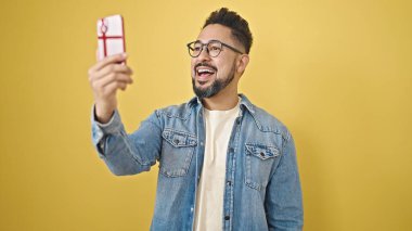 Genç Latin adam gülümsüyor. İzole edilmiş sarı arka planda video araması yaptırıyor.