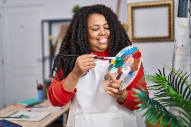 African american woman artist holding paintbrush and palette at art studio