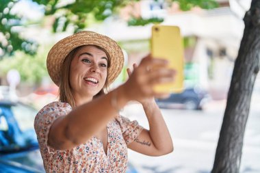 Yaz şapkası takan genç bir turist sokakta video görüşmesi yapıyor.