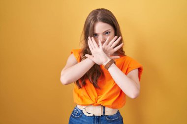 Beyaz kadın sarı arka planda duruyor. Reddedilme ifadesi. Kollar ve avuç içleri kesişiyor. 