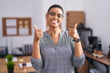 Ofiste çalışan Afro-Amerikalı bir kadın gözlük takıyor. Elleriyle olumlu jest yapıyor. Gülümsüyor ve başarı için seviniyor. kazanan jest. 