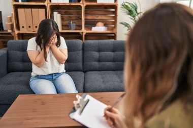 Down sendromlu İspanyol kız ağlarken yüzünü ellerle kapatan üzgün bir ifadeyle terapi yapıyor. depresyon kavramı. 