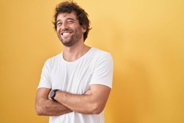 Young hispanic man standing with arms crossed gesture over isolated yellow background