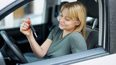 Genç sarışın kadın gülümsüyor. Elinde yeni arabanın anahtarı var.