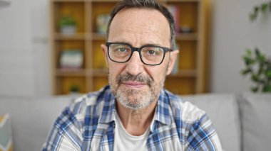 Middle age man sitting on sofa with relaxed expression at home