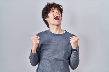 Young man standing over isolated background celebrating surprised and amazed for success with arms raised and eyes closed. winner concept. 
