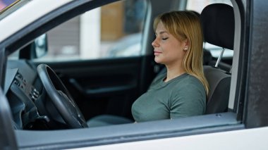 Sokakta rahat bir ifadeyle araba süren genç sarışın kadın.