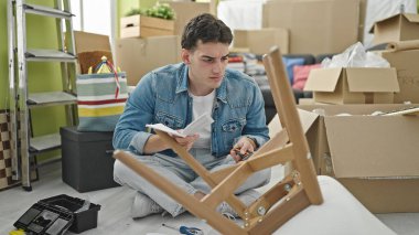 Genç İspanyol adam yeni evindeki sandalyeyi tamir etme talimatlarını okuyor.