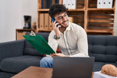 Genç İspanyol Psikolog elinde dosya olan akıllı telefondan konuşuyor.