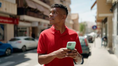 Young latin man using smartphone with serious expression at street