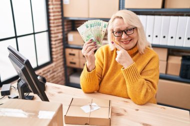 Orta yaşlı beyaz kadın küçük işletmelerde çalışıyor elinde Hong Kong dolarları tutarak mutlu mesut parmakla işaret ediyor. 