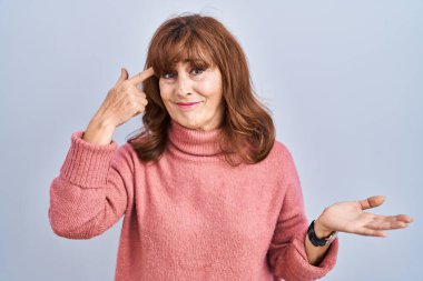 Middle age hispanic woman standing over isolated background confused and annoyed with open palm showing copy space and pointing finger to forehead. think about it. 