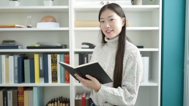 Young chinese woman student reading book studying at library university