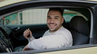 Young hispanic man smiling confident holding key of new car at street