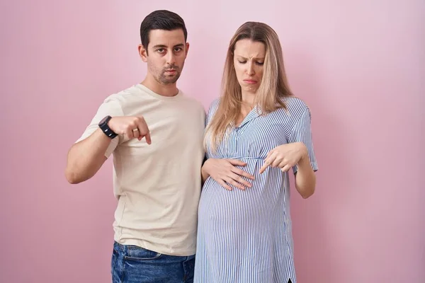 Casal Jovem Esperando Bebê Sobre Fundo Rosa Apontando Para Baixo — Fotografia de Stock