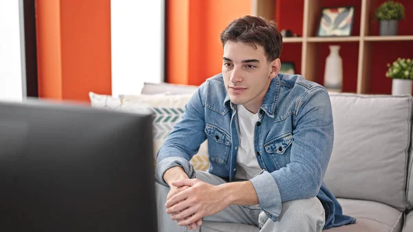 Joven Hombre Hispano Viendo Televisión Sentada Sofá Con Expresión Relajada —  Fotos de Stock