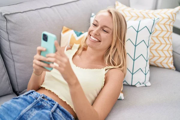 Młoda Blondynka Pomocą Smartfona Leżącego Kanapie Domu — Zdjęcie stockowe