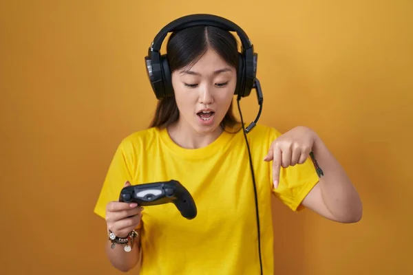 中国年轻女子正在玩电子游戏 手里拿着控制器 手指垂下 展示广告 惊讶的脸和张开的嘴 — 图库照片