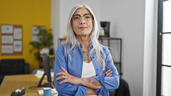 Middle age grey-haired woman business worker standing with arms crossed gesture at office